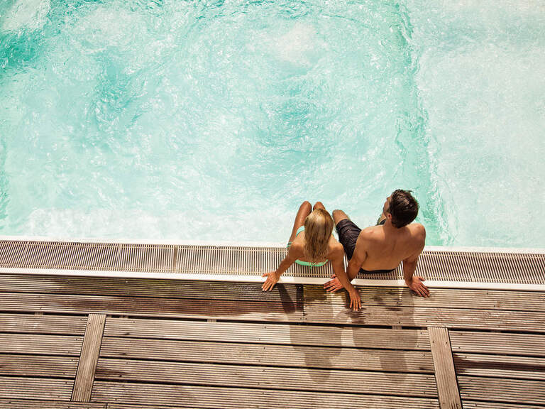 Ein Paar sitzt entspannt am Rand eines Pools in einem Thermalbad von Bad Füssing.